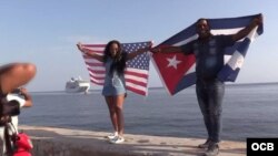 Dos cubanos, con las banderas de Cuba y Estados Unidos, esperan la llegada del Adonia en el Malecón habanero. 
