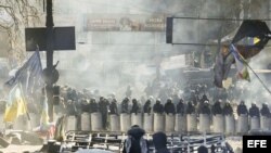 Varios manifestantes permanecen tras una barricada ante un cordón policial en Kiev (Ucrania). Archivo.