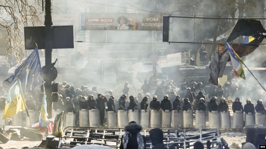 Varios manifestantes permanecen tras una barricada ante un cordón policial en Kiev (Ucrania). Archivo.