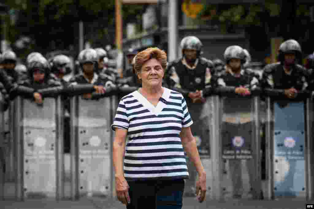  Una mujer camina cerca a policías antimotines mientras estudiantes opositores al Gobierno y profesores universitarios protestan en Caracas (Venezuela). 