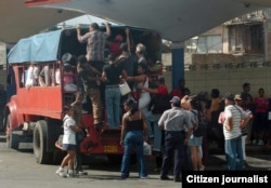 Varias personas intentan subir a un camión particular que funciona como transporte público.