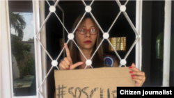 Iliana Hernández, atrapada en su hogar, con un cartel de #SOSCUBA. 