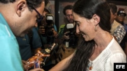 La disidente cubana Yoani Sánchez (d), autora del blog "Generación Y", recibe del cineasta Dado Galvao (i), su anfitrión en Brasil, una cinta de "Senhor do Bonfim" hoy, lunes 18 de febrero de 2013, en el aeropuerto internacional Guararapes, de la ciudad d