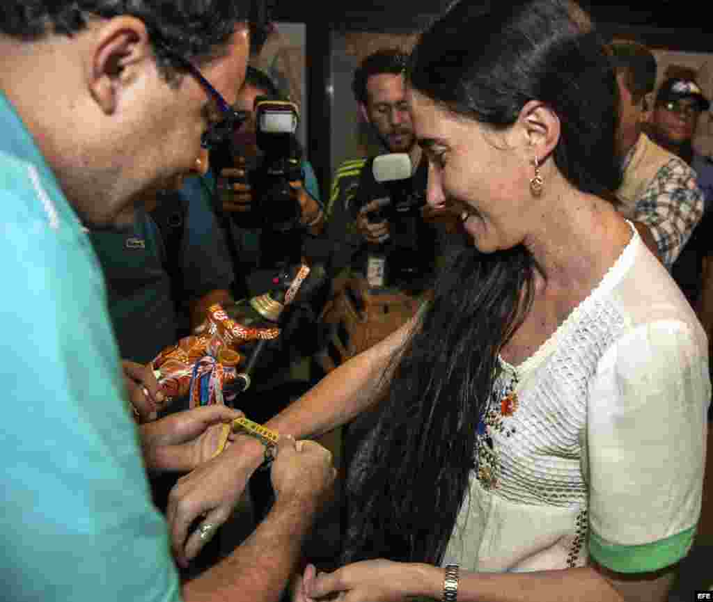 La disidente cubana Yoani Sánchez (d), autora del blog "Generación Y", recibe del cineasta Dado Galvao (i), su anfitrión en Brasil, una cinta de "Senhor do Bonfim" hoy, lunes 18 de febrero de 2013, en el aeropuerto internacional Guararapes, de la ciudad d