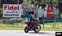 Dos personas en moto pasan junto a un cartel donde aparece el líder de la revolución cubana, Fidel Castro.