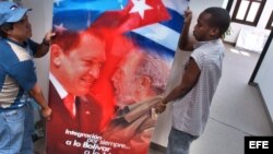 Dos obreros trasladan un cristal con la imagen de Hugo Chávez y Fidel Castro.