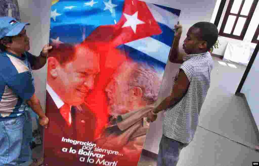 Dos obreros trasladan un cristal con la imagen de Hugo Chávez y Fidel Castro.