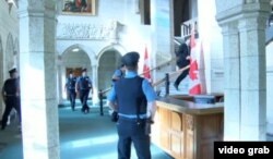 Personal de seguridad armado sube las escaleras del parlamento canadiense en pos del asesino de un soldado (CBC).