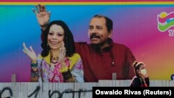 Una mujer con un cubreboca pasa por delante de una valla con imágenes del presidente Daniel Ortega y su esposa Rosario Murillo en Managua, Nicaragua. REUTERS/Oswaldo Rivas