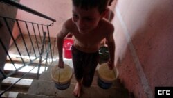  Un niño carga dos cubos de agua por las escaleras de su casa. 