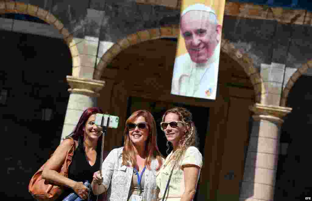 Tres mujeres se toman una "selfie" junto a un cartel con la imagen del papa Francisco, en La Habana. EFE