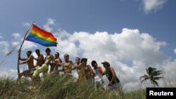 Un grupo de hombres posa con la bandera del movimiento gay en una playa de Cuba.