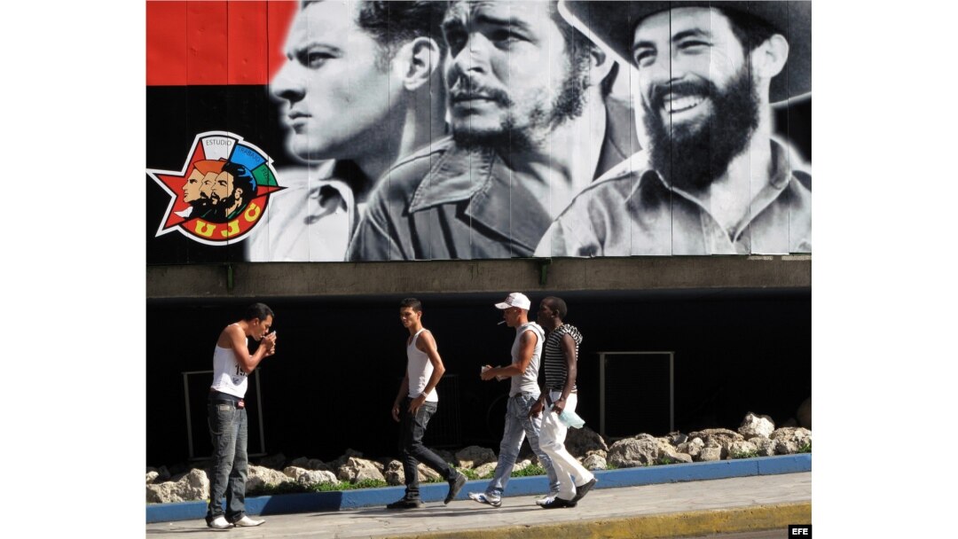 Un grupo de jóvenes camina frente a un cartel alusivo a la Unión de Jóvenes Comunistas (UJC).