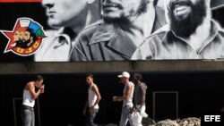 Un grupo de jóvenes camina frente a un cartel alusivo a la Unión de Jóvenes Comunistas (UJC).