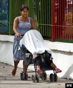 Una mujer camina con un niño, en un coche para bebé en La Habana.