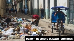Un conductor de bicitaxi espera a los clientes junto a un montón de basura en La Habana, Cuba, el lunes 1 de junio de 2026. (Foto AP/Ramón Espinosa)