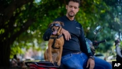 El perro rescatado Koffee se sienta en una motocicleta junto a su nuevo dueño, Leandro Valdés, durante una entrevista en La Habana. (AP Foto/Ramón Espinosa)