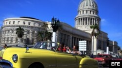 Dos turistas viajan en un viejo auto descapotable por una calle de La Habana. 