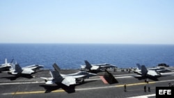 Miembros de la Marina guiando a varios aviones Hornet F/A 18 para su despegue desde la cubierta de un portaaviones estadounidense.