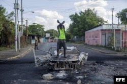 Un hombre protesta encima de un vehículo quemado en una calle de Managua.
