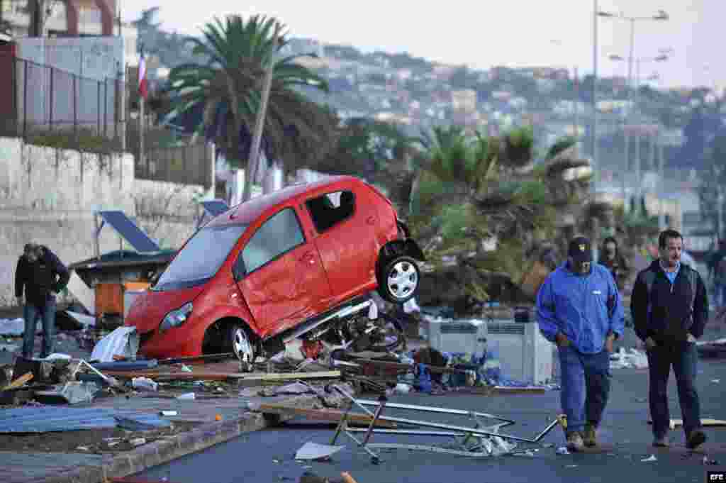 Dos hombres caminan frente a un vehículo arrastrado por el tsunami que siguió al terremoto en Chile.