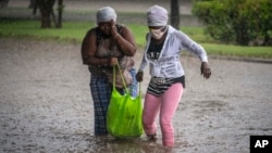 Cubanas tratan de cruzar una calle inundada por la lluvia.