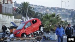 Dos hombres caminan frente a un vehículo arrastrado por el tsunami que siguió al terremoto en Chile.