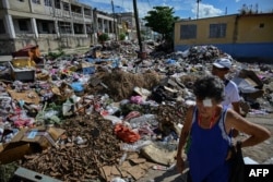 Personas caminan junto a montones de basura sin recoger en una calle de La Habana, Cuba, el 26 de octubre de 2026. YAMIL LAGE / AFP