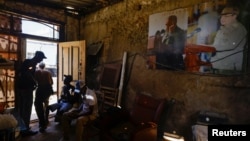 Varias personas conversan en el interior de una carpintería, junto a un cartel de los dictadores Fidel Castro y Raúl Castro, en La Habana, Cuba, 20 de mayo de 2026. REUTERS/Norlys Perez