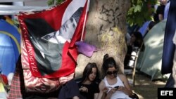 Dos activistas sentadas bajo un árbol observan un teléfono móvil, junto a una bandera del fundador de la República, Mustafa Kemal Ataturk, en el parque Gezi de Estambul, Turquía