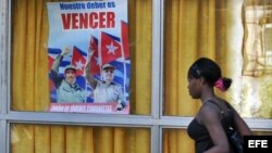 Una joven cubana camina junto a un cartel alusivo a los líderes de la revolución cubana, Fidel y Raúl Castro.