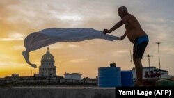 Alexis Miján estira las sábanas de una cama improvisada en la azotea de un edificio residencial al atardecer en La Habana Vieja.