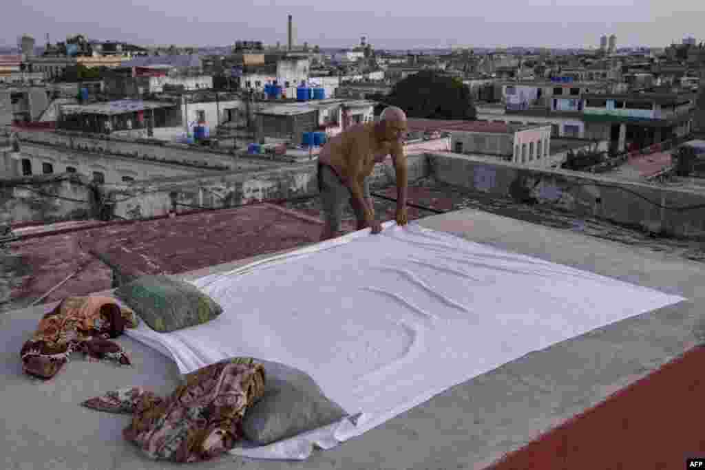 Alexis Miranda extiende una sábana sobre la azotea de un edificio residencial al atardecer en La Habana Vieja, el 11 de agosto de 2026. Muchos cubanos duermen al aire libre durante las noches de verano buscando alivio ante las altas temperaturas y los frecuentes cortes de electricidad. YAMIL LAGE / AFP.