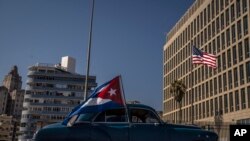 Un carro que sostiene una bandera de Cuba pasa por la Embajada de EEUU en La Habana. (AP Photo/Ramón Espinosa).