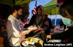 Un migrante, centro, recibe una comida caliente de parte de voluntarios afuera de la Iglesia del Sagrado Corazón en el centro de El Paso, Texas, el sábado 7 de enero de 2023. (AP/Andres Leighton)