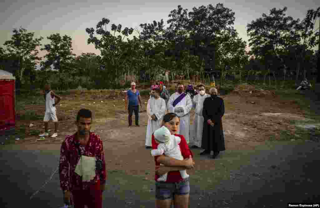 Una madre carga a su bebé en brazos mientras religiosos católicos observan la peregrinación en La Habana al Santuario dedicado al santo en El Rincón, Santiago de las Vegas. (AP/Ramon Espinosa)