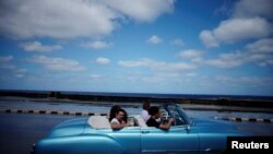 Turistas pasean por el Malecón de La Habana en un auto clásico americano. 
