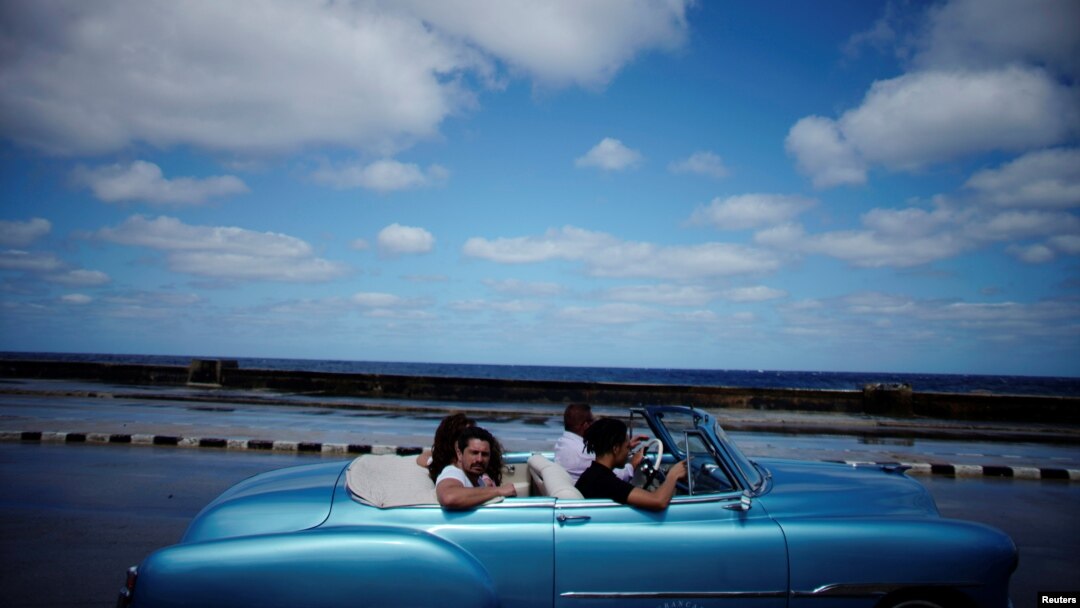 Turistas pasean por el Malecón de La Habana en un auto clásico americano. 