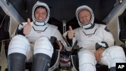 Los astronautas Robert Behnken (izq.) y Douglas Hurley saludan a su regreso a la Tierra dentro de la cápsula SpaceX Dragon.
