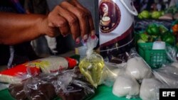 Una vendedora informal sostiene una bolsa de aceite vegetal, que ofrece a la venta junto a azúcar y café en un puesto en una calle de Caracas.