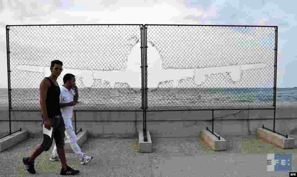 Dos hombres caminan junto a la obra &quot;Fly away&quot;, del artista cubano Arl&eacute;s del R&iacute;o.