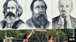 Dos turistas posan junto a carteles con los rostros de Marx, Engels y Lenin en la Plaza de la Revolución de La Habana.