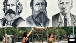 Dos turistas posan junto a carteles con los rostros de Marx, Engels y Lenin en la Plaza de la Revolución de La Habana.
