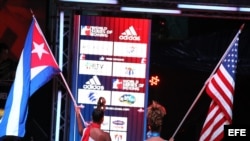 Dos mujeres caminan con las banderas de Cuba y Estados Unidos al comienzo del enfrentamiento entre el equipo "Domadores de Cuba" y USA knockouts por la serie mundial de boxeo.