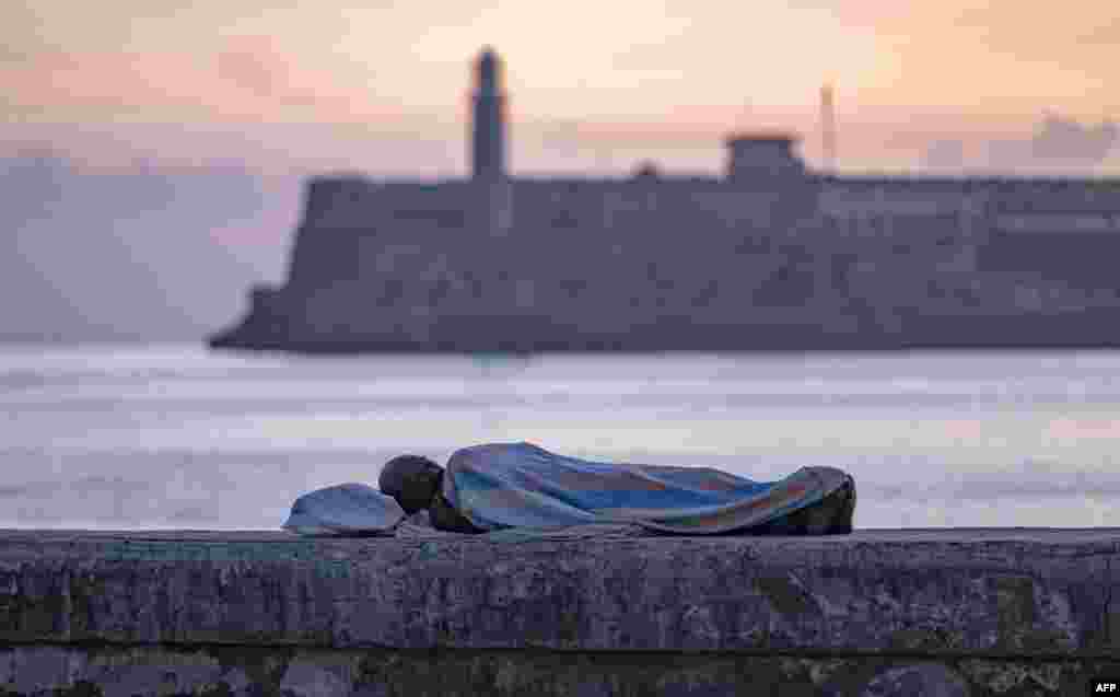 Una persona duerme envuelta en una sábana sobre el muro del Malecón al amanecer en La Habana, el 13 de agosto de 2026. YAMIL LAGE / AFP