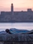 Una persona duerme envuelta en una sábana sobre el muro del Malecón al amanecer en La Habana, el 13 de agosto de 2026. YAMIL LAGE / AFP