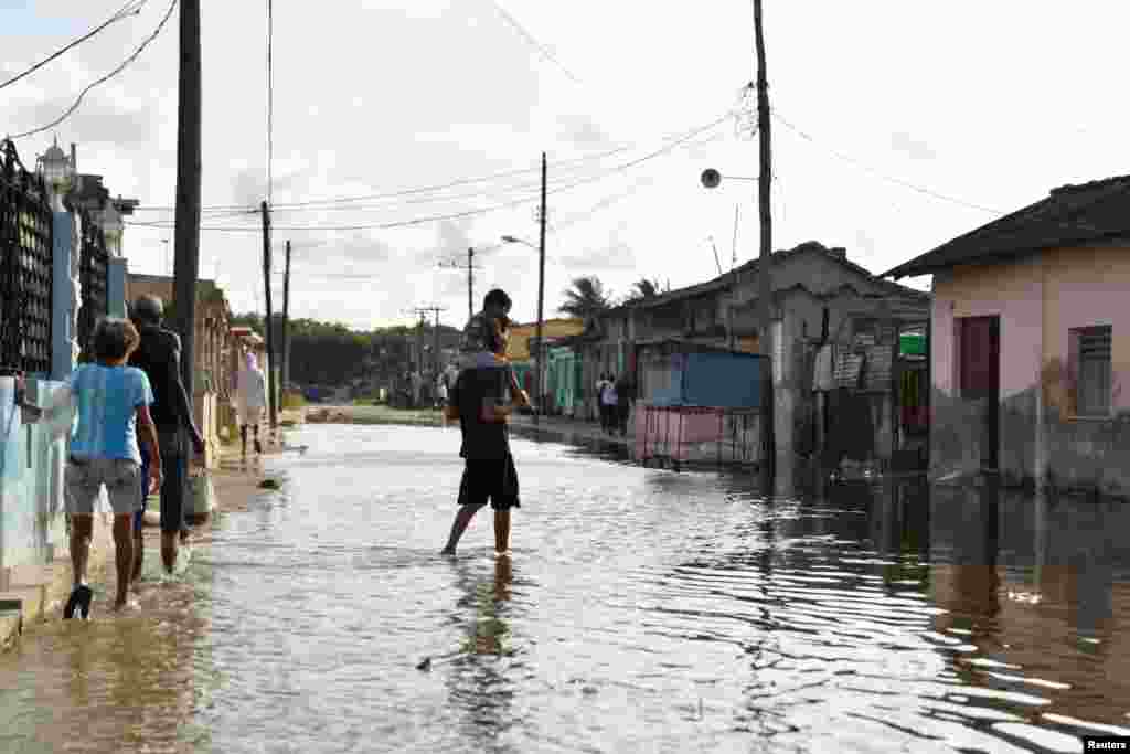 Un hombre carga a un niño por una calle inundada mientras el huracán Milton se acercaba a la costa cubana en Batabanó. REUTERS/Norlys Pérez