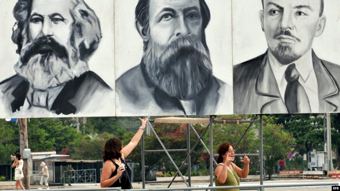 Dos turistas posan junto a carteles con los rostros de Marx, Engels y Lenin en la Plaza de la Revolución de La Habana.