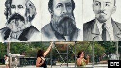 Dos turistas posan junto a carteles con los rostros de Marx, Engels y Lenin en la Plaza de la Revolución de La Habana.