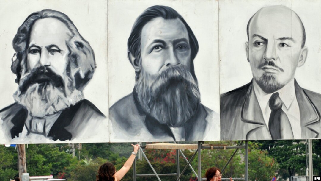 Dos turistas posan junto a carteles con los rostros de Marx, Engels y Lenin en la Plaza de la Revolución de La Habana.